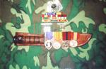 Dogtags, service ribbons, medals, and Ka-Bar knife associated with Thomas Belton�s military service. Service ribbons (L-R): Purple Heart, Combat Action, National Defense, Meritorious Service, Good Conduct, Navy Unit Commendation, Vietnam Service with fo