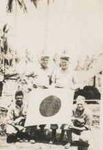 Left to right: standing: George Mackie and John J. Higgins. squatting: Hank Freageu and Steve Kroll Holding a Japanese flag, which indicates a plane was shot down, New Guinea, September 1944